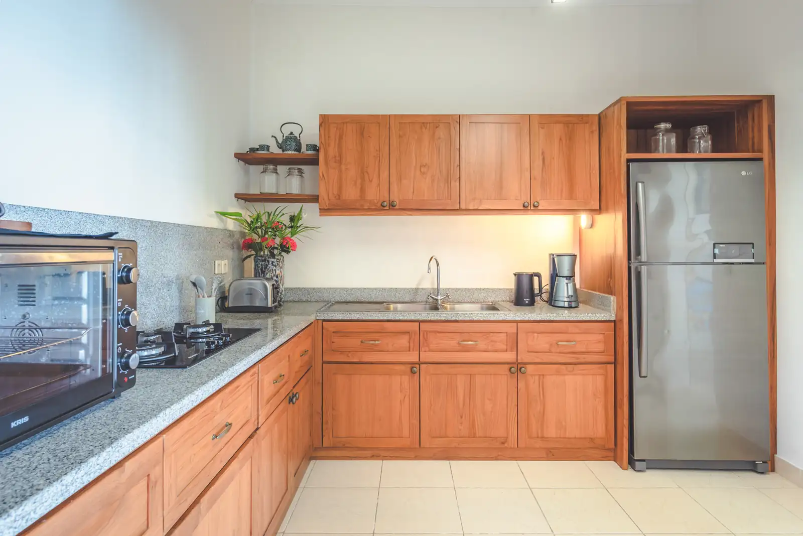 Fully equipped kitchen with teakwood cabinets, granite countertop, gas hob, and oven at Primavera Beach House.