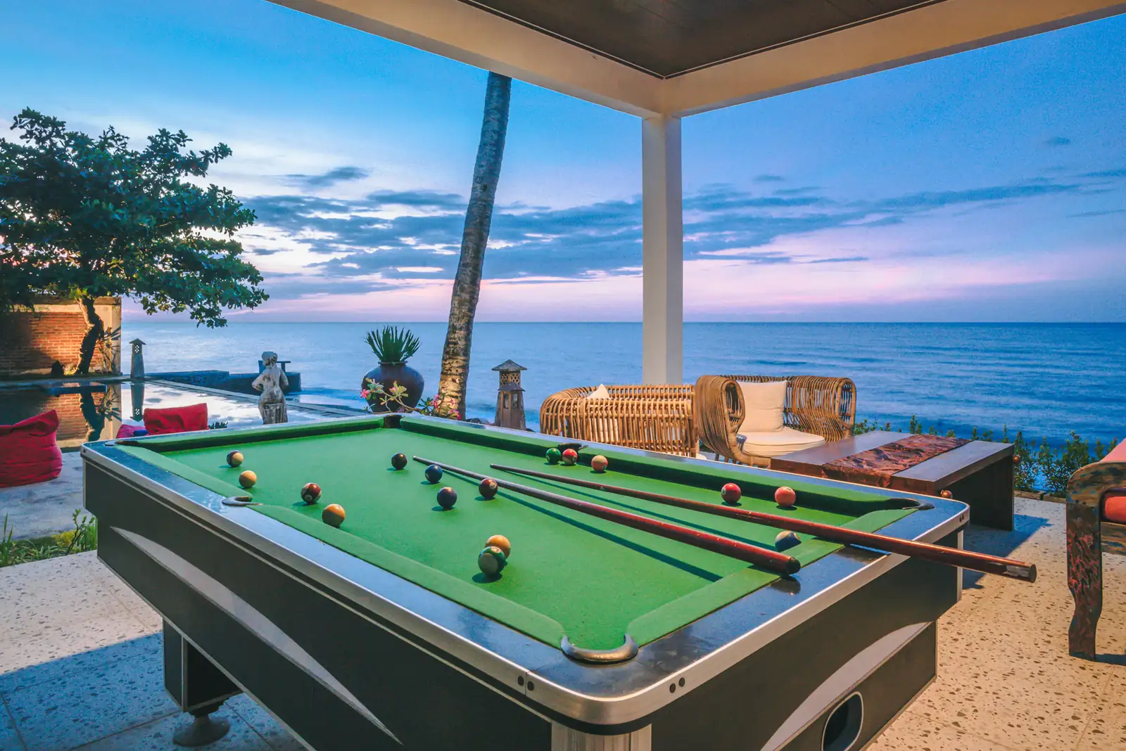 Billiard table under the seafront pavilion at blue hour, with balls and cues laid out and the Bali Sea behind, Primavera Beach House.