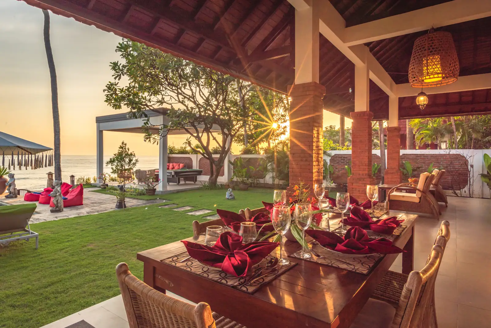 Table set for dinner on the covered terrace at sunset, with billiard table visible in the background, Primavera Beach House.
