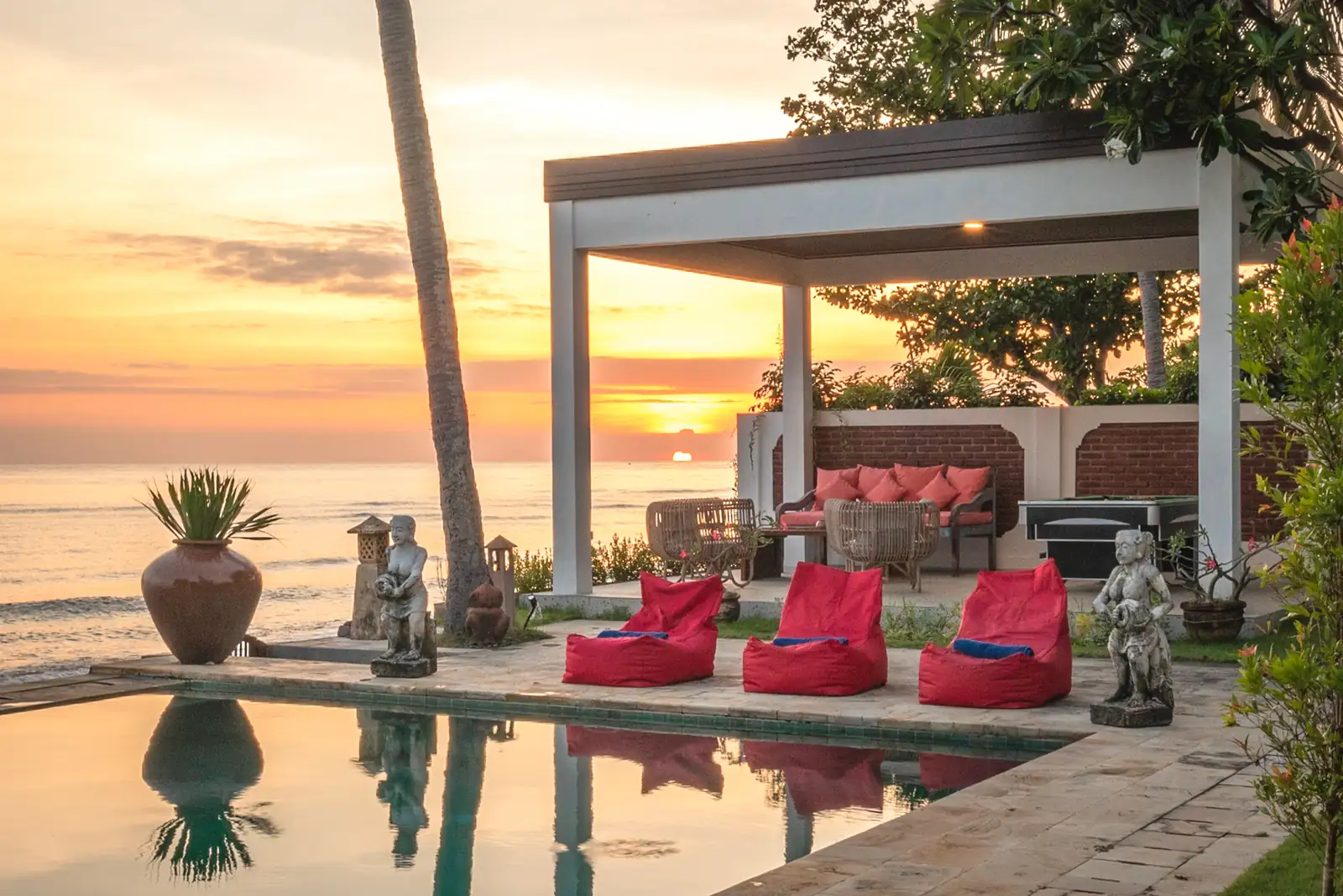 Sunset over the pool and beachfront bale with beanbags and Balinese stone statues.
